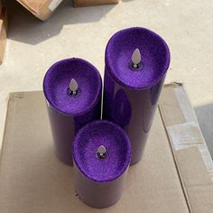 three purple candles sitting on top of a cardboard box