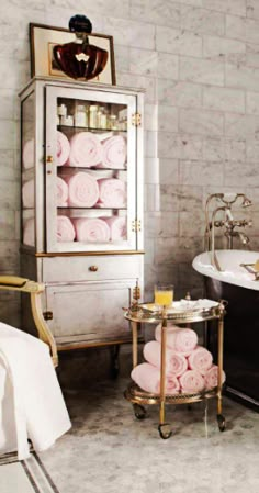 an old fashioned bathtub in a bathroom with pink towels on the shelf and mirror