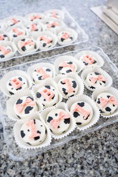 some cupcakes with pink bows on them are sitting in plastic trays next to each other