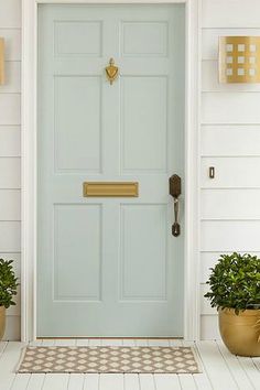 two potted plants sit in front of a blue door on a white house with gold accents