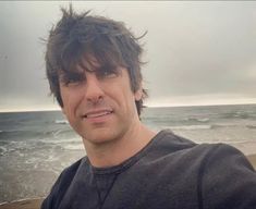 a man standing on top of a beach next to the ocean with waves coming in