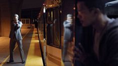 a man standing next to a train at night with his cell phone in his hand