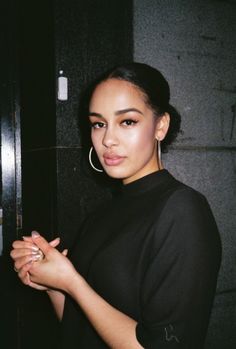 a woman with large hoop earrings standing in front of a black wall and looking at the camera