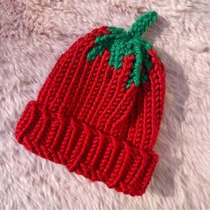 a knitted strawberry hat laying on top of a white furnishing area,