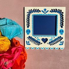 there is a blue and white frame on the wall next to some colorful cloths