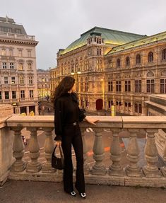 a woman standing on top of a bridge next to tall buildings and looking at the sky