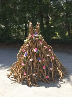 a sculpture made out of branches and flowers on the ground in front of some trees