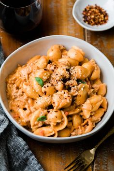 a white bowl filled with pasta and sauce on top of a wooden table next to a cup of coffee