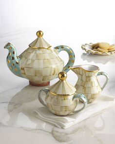 three pieces of ceramic tea set on a white tablecloth with cookies in the background