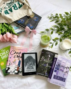 some books are laying on a bed with pink tulips and green plants next to it