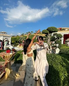 a man and woman walking down a path in front of some bushes with their hands up