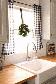 a kitchen sink sitting under a window next to a wooden counter top with a wreath on it