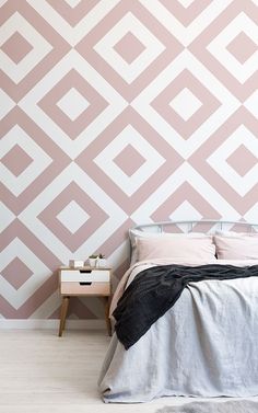 a bed sitting under a pink and white wall next to a night stand with a lamp on it