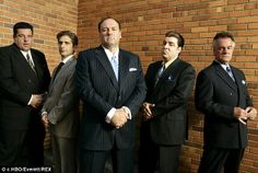 four men standing in front of a brick wall wearing suits and ties with their arms crossed