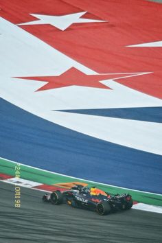 a red and blue race car driving on a track with stars painted on the wall behind it