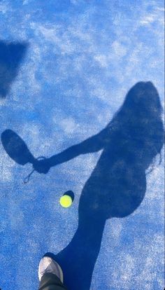 the shadow of a woman holding a tennis racquet and ball on a tennis court