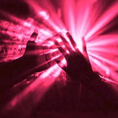 a person holding their hand out in front of a red and black background with beams of light