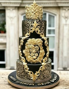 a three tiered black and gold wedding cake with a lion head on the top