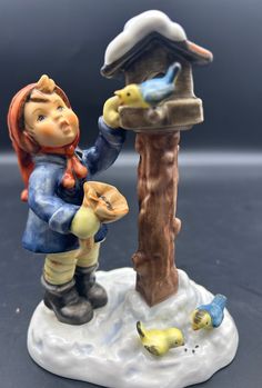 a ceramic figurine of a girl holding a bird feeder with birds around it