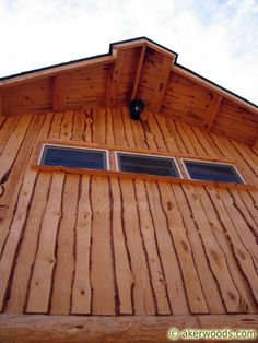 the side of a wooden building with three windows on each window sill and a sky background