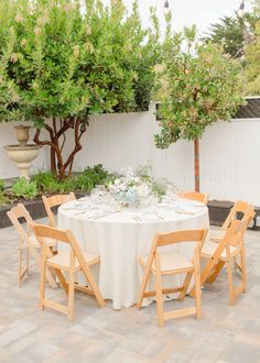 the table is set with white linens and wooden chairs for an outdoor dinner party