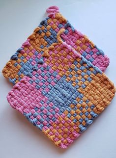 a crocheted dishcloth is displayed on a white surface with pink, blue and yellow squares