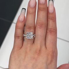 a woman's hand with white and black nail polish holding a square shaped diamond ring