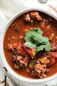 a white bowl filled with chili and meat stew on top of a table next to a spoon