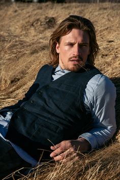 a man laying on the ground with his hands in his pockets and wearing a vest