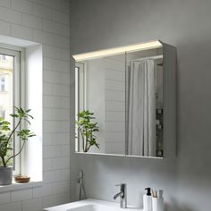 a bathroom sink sitting under a mirror next to a plant in a window sill