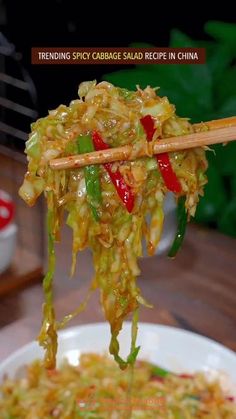 chopsticks holding up noodles in a bowl with vegetables and sauce on the side