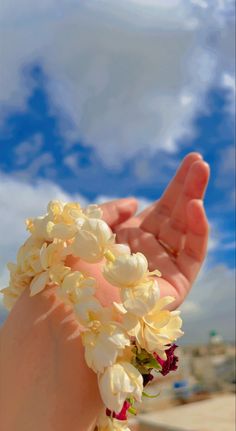 a person's hand holding flowers in front of a blue sky with white clouds