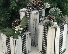 four wooden boxes decorated with pine cones and plaid bows are sitting on the ground in front of evergreens