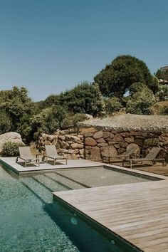 a wooden deck next to a swimming pool with lounge chairs on it and trees in the background