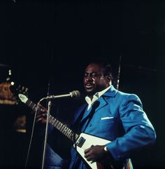 a man in a blue suit playing an electric guitar and singing into a microphone on stage