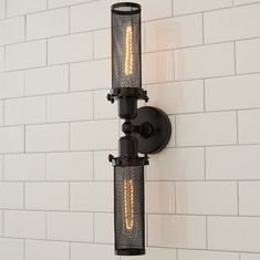 two lights are attached to the side of a white brick wall in an industrial - style bathroom