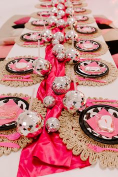 the table is set with pink and black plates, napkins, and silver balls