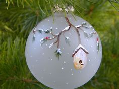 a glass ornament with a birdhouse on it hanging from a pine tree