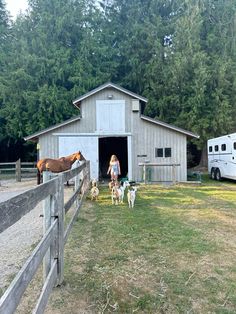 a woman standing in front of a barn with two dogs and three horses next to it