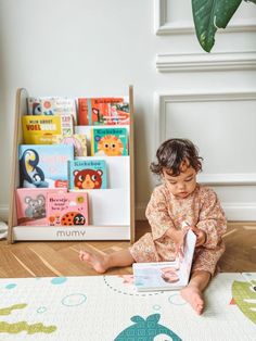 a toddler sitting on the floor reading a book in front of bookshelves