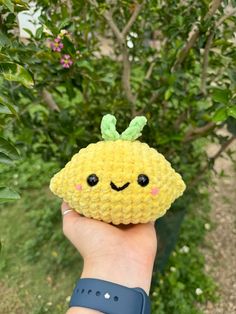 a hand holding up a small yellow crocheted object with a smiley face on it