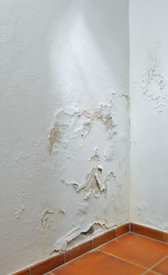 the corner of a room with peeling paint on the wall and tile flooring in front of it