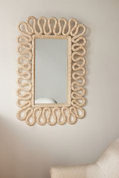 a mirror hanging on the wall next to a white chair and striped pillow in a room