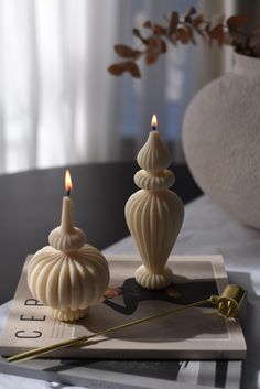 two white candles sitting on top of a magazine