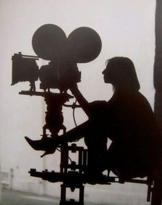 a man sitting in front of a camera on top of a tripod next to a window