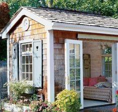 a small wooden shed sitting in the middle of a yard with lots of flowers around it