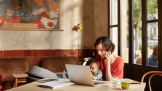 a woman sitting at a table with a baby on her lap while using a laptop