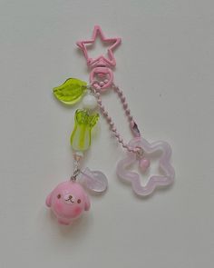 two pacifiers with charms attached to them on a white surface, one pink and one green