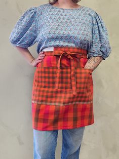 a woman wearing an orange and blue checkered apron with her hands on her hips