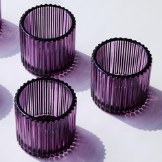 four purple glass vases sitting next to each other on top of a white surface